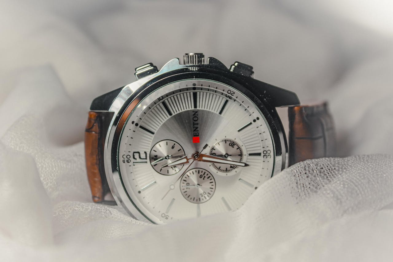 services-03 Close-up of a stylish analog watch with brown leather strap over soft fabric.