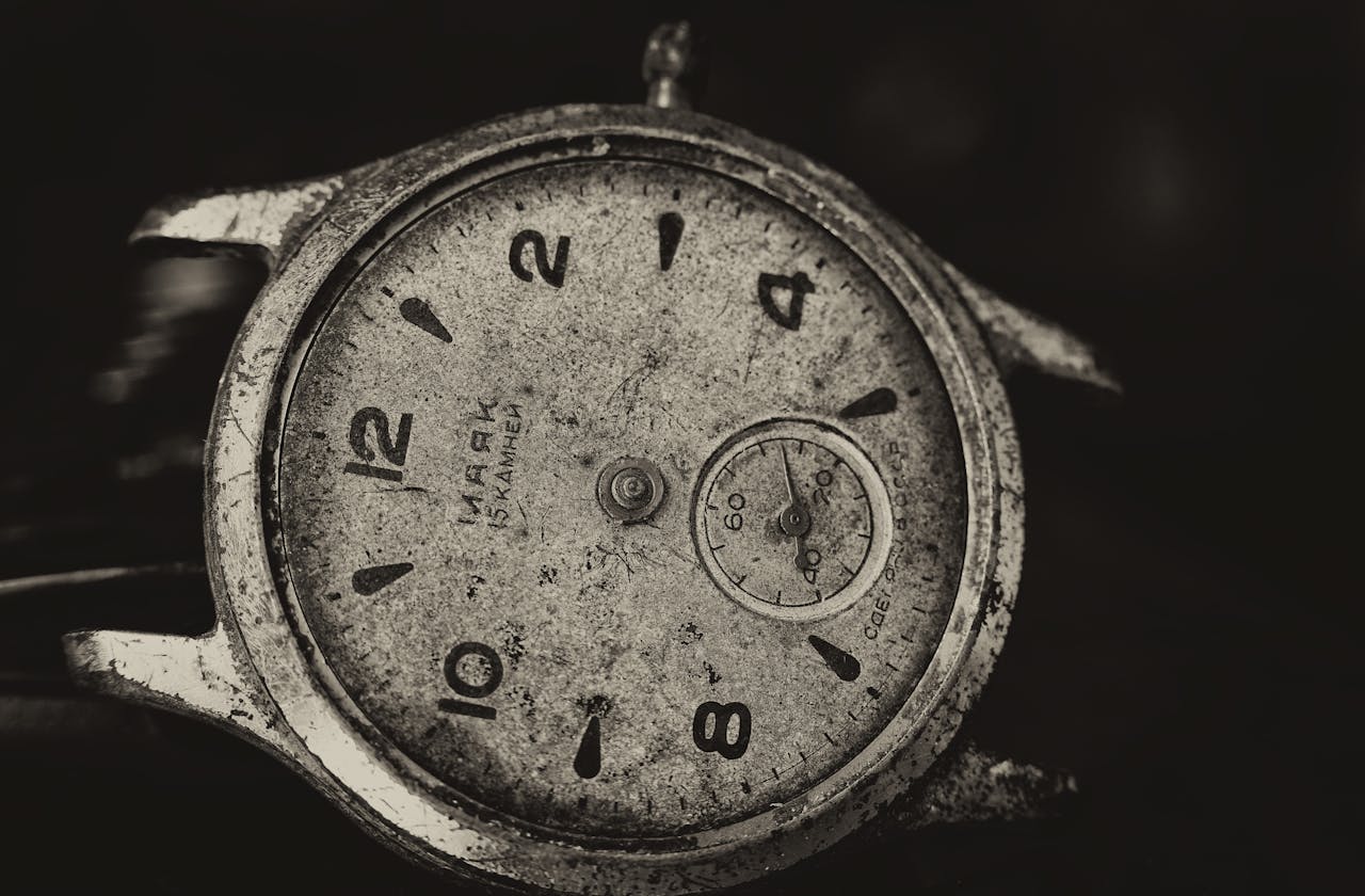 A detailed black and white close-up image of an old broken wristwatch showing aged texture and wear.